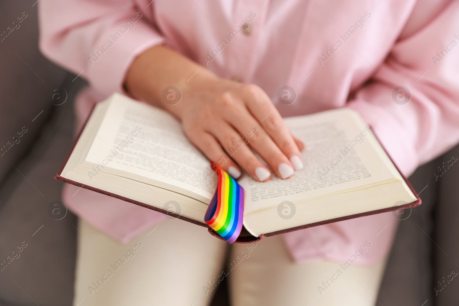 Photo of Woman with ribbon in LGBT colors reading book indoors, closeup