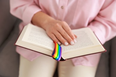 Photo of Woman with ribbon in LGBT colors reading book indoors, closeup