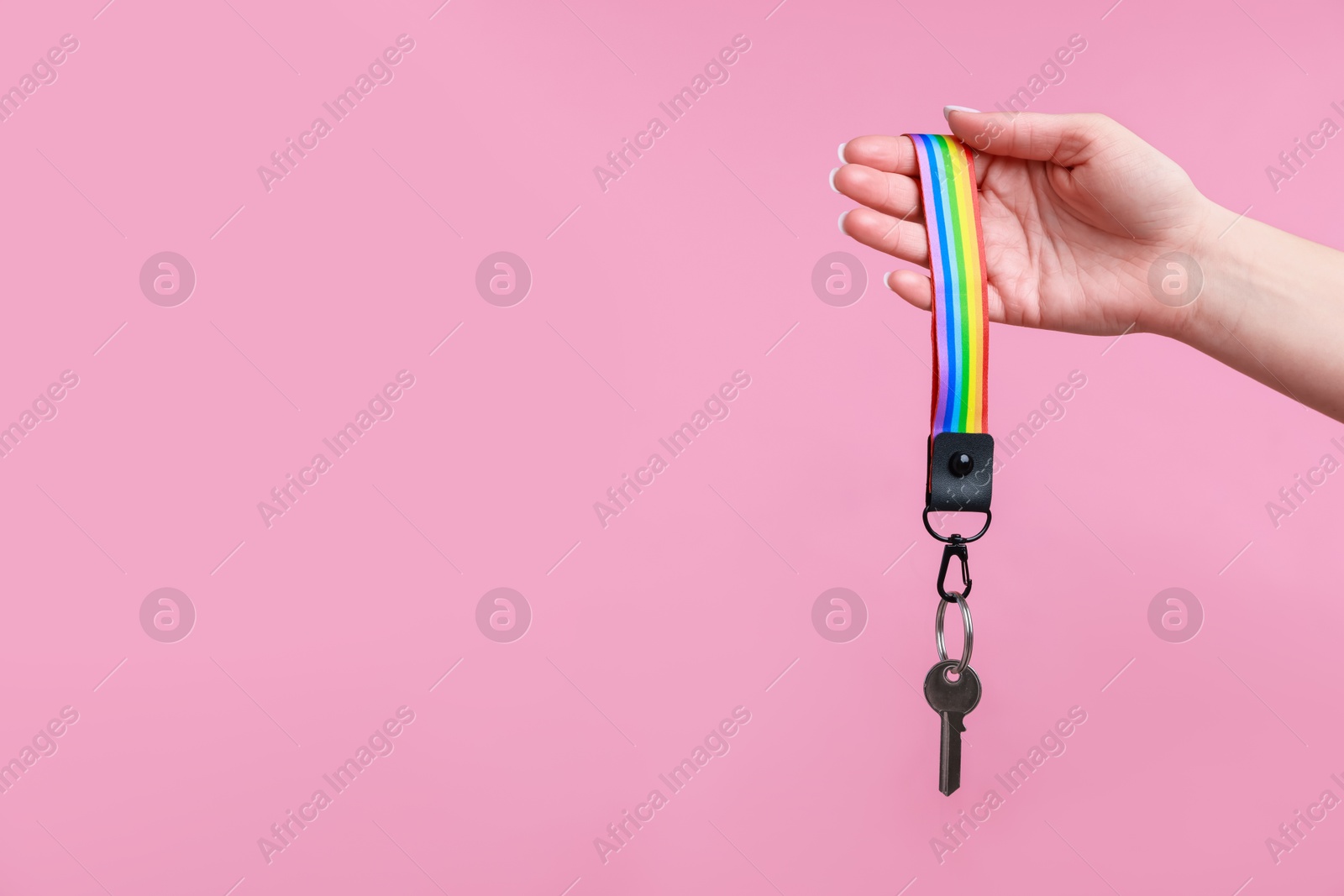 Photo of Woman holding key with keychain in LGBT colors on pink background, closeup. Space for text