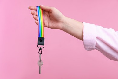 Photo of Woman holding key with keychain in LGBT colors on pink background, closeup