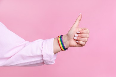 Photo of Woman wearing wristband in LGBT colors and showing thumbs up on pink background, closeup