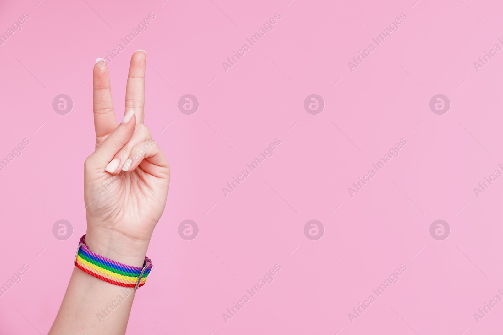 Photo of Woman wearing wristband in LGBT colors and showing peace sign on pink background, closeup. Space for text