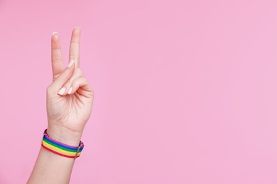 Photo of Woman wearing wristband in LGBT colors and showing peace sign on pink background, closeup. Space for text