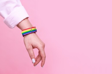 Photo of Woman wearing wristband in LGBT colors on pink background, closeup. Space for text