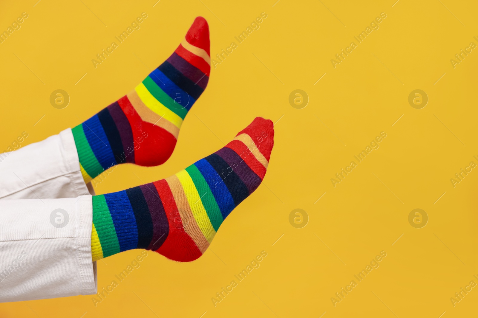 Photo of Woman wearing socks in LGBT colors on orange background, closeup. Space for text