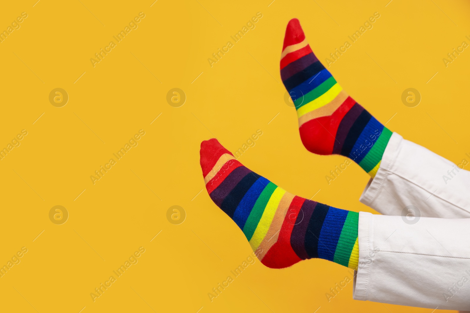 Photo of Woman wearing socks in LGBT colors on orange background, closeup. Space for text