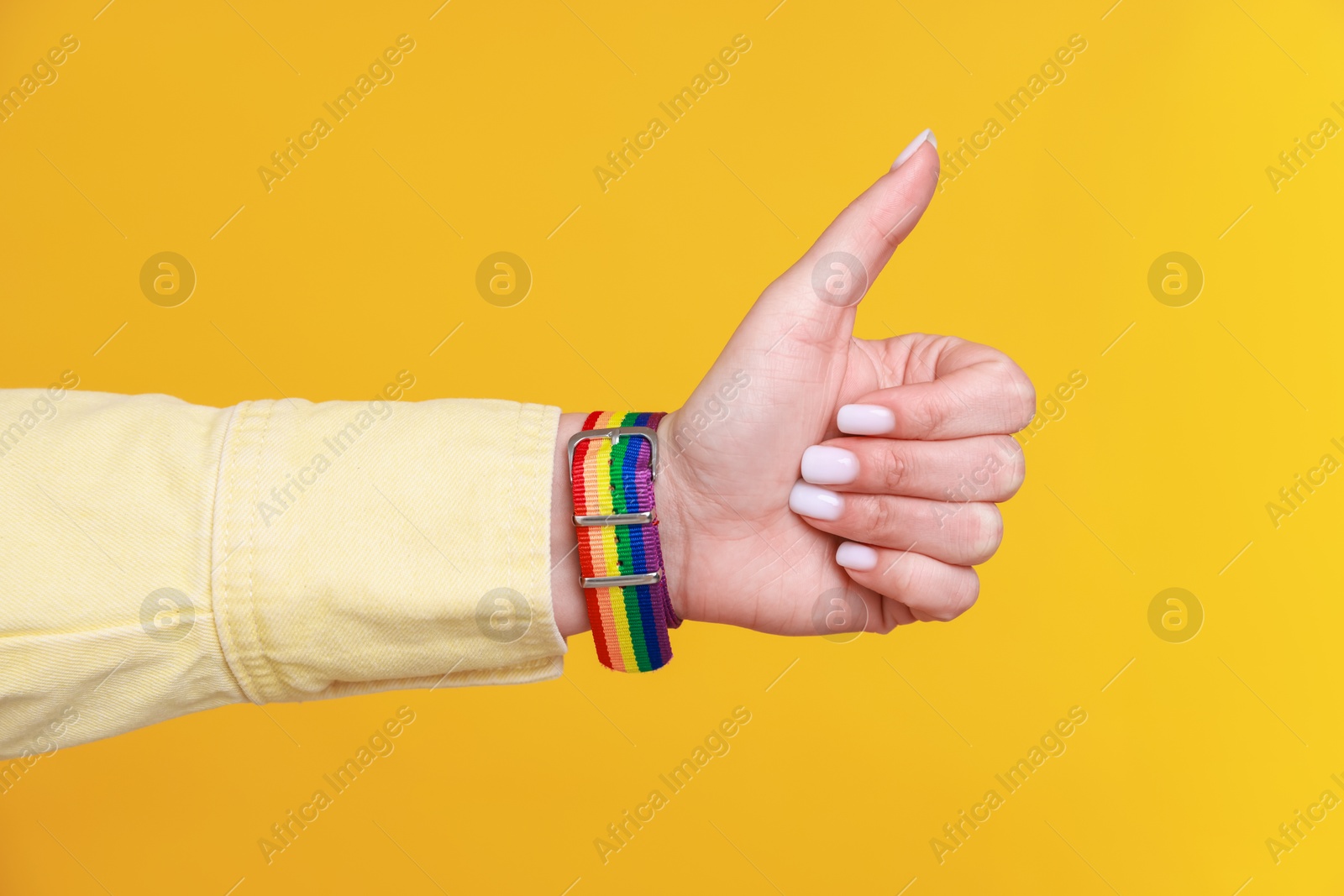 Photo of Woman wearing wristband in LGBT colors and showing thumbs up on orange background, closeup