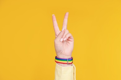 Photo of Woman wearing wristband in LGBT colors and showing peace sign on orange background, closeup