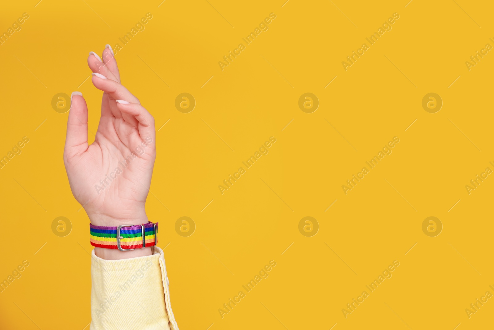 Photo of Woman wearing wristband in LGBT colors on orange background, closeup. Space for text