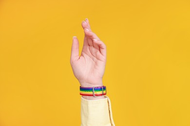 Photo of Woman wearing wristband in LGBT colors on orange background, closeup