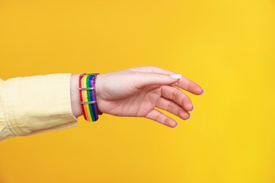 Photo of Woman wearing wristband in LGBT colors on orange background, closeup