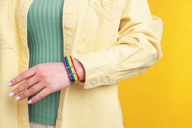 Photo of Woman wearing wristband in LGBT colors on orange background, closeup