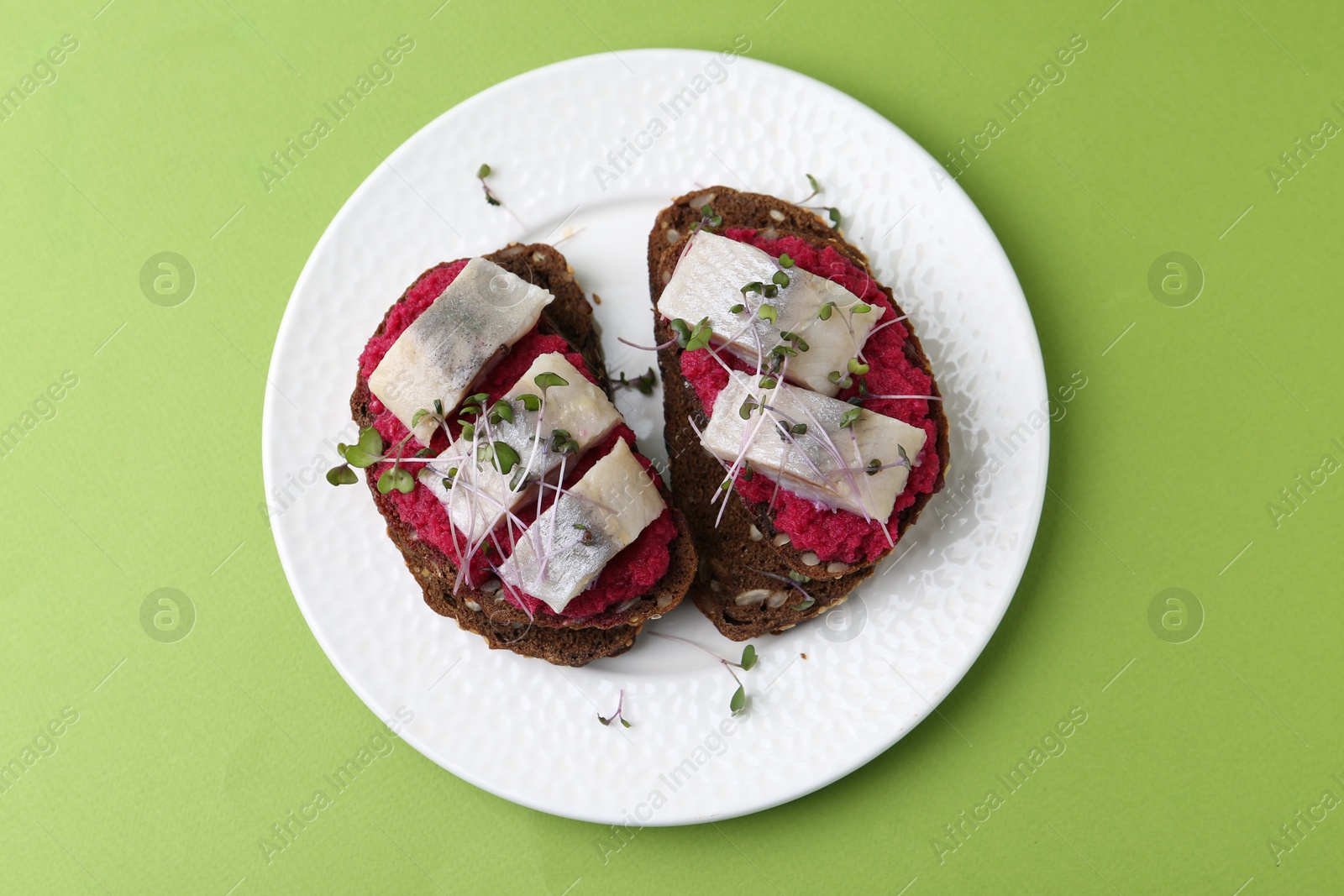 Photo of Tasty sandwiches with herring and horseradish sauce on green background, top view