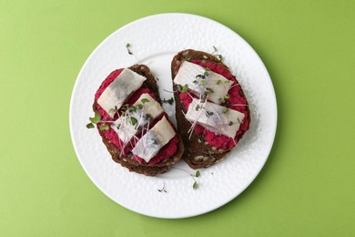 Tasty sandwiches with herring and horseradish sauce on green background, top view