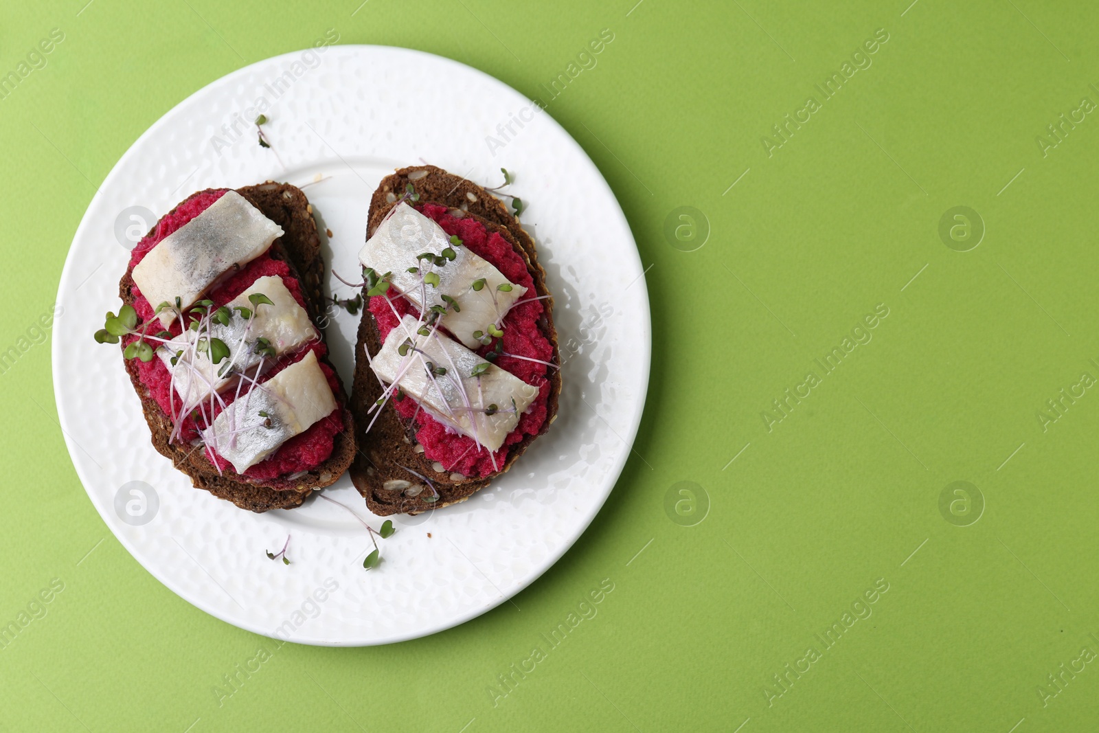 Photo of Tasty sandwiches with herring and horseradish sauce on green background, top view. Space for text