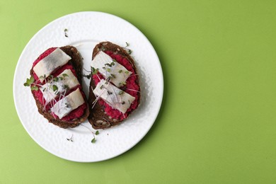 Tasty sandwiches with herring and horseradish sauce on green background, top view. Space for text