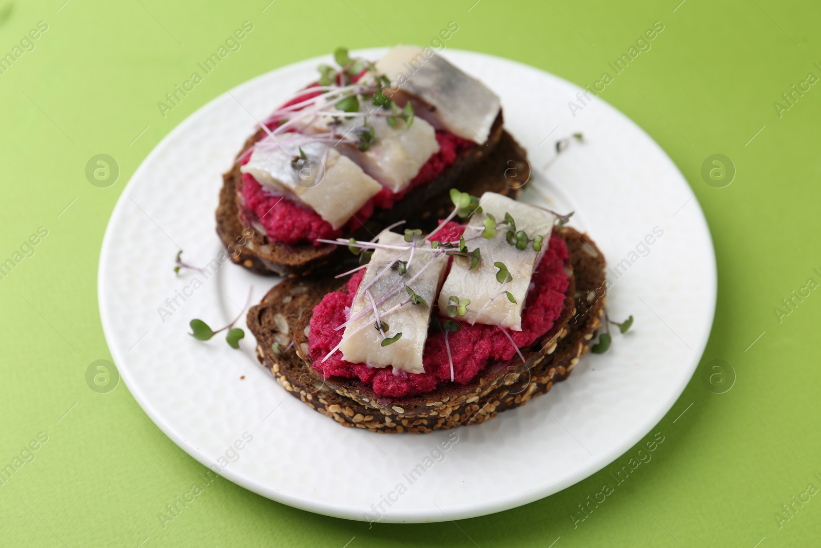 Photo of Tasty sandwiches with herring and horseradish sauce on green background, closeup