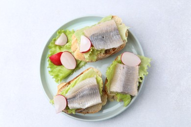 Photo of Tasty sandwiches with herring, radish and lettuce on light table, top view