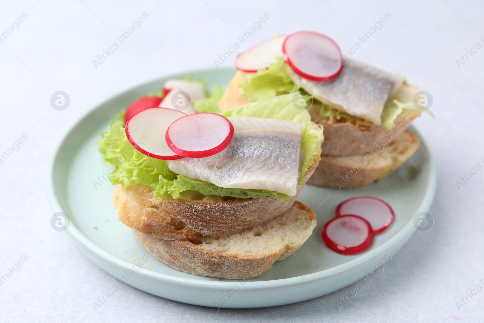 Photo of Tasty sandwiches with herring, radish and lettuce on light table, closeup