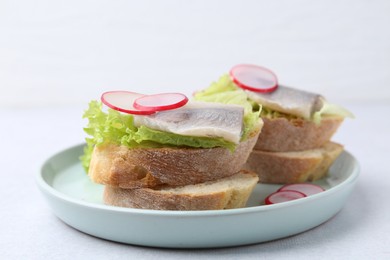 Photo of Tasty sandwiches with herring, radish and lettuce on light table, closeup