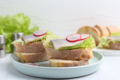 Photo of Tasty sandwiches with herring, radish and lettuce on white table, closeup