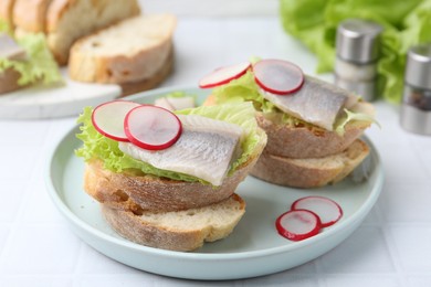 Photo of Tasty sandwiches with herring, radish and lettuce on white tiled table, closeup