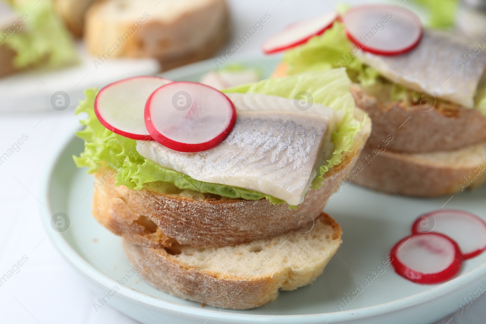 Photo of Tasty sandwiches with herring, radish and lettuce on table, closeup