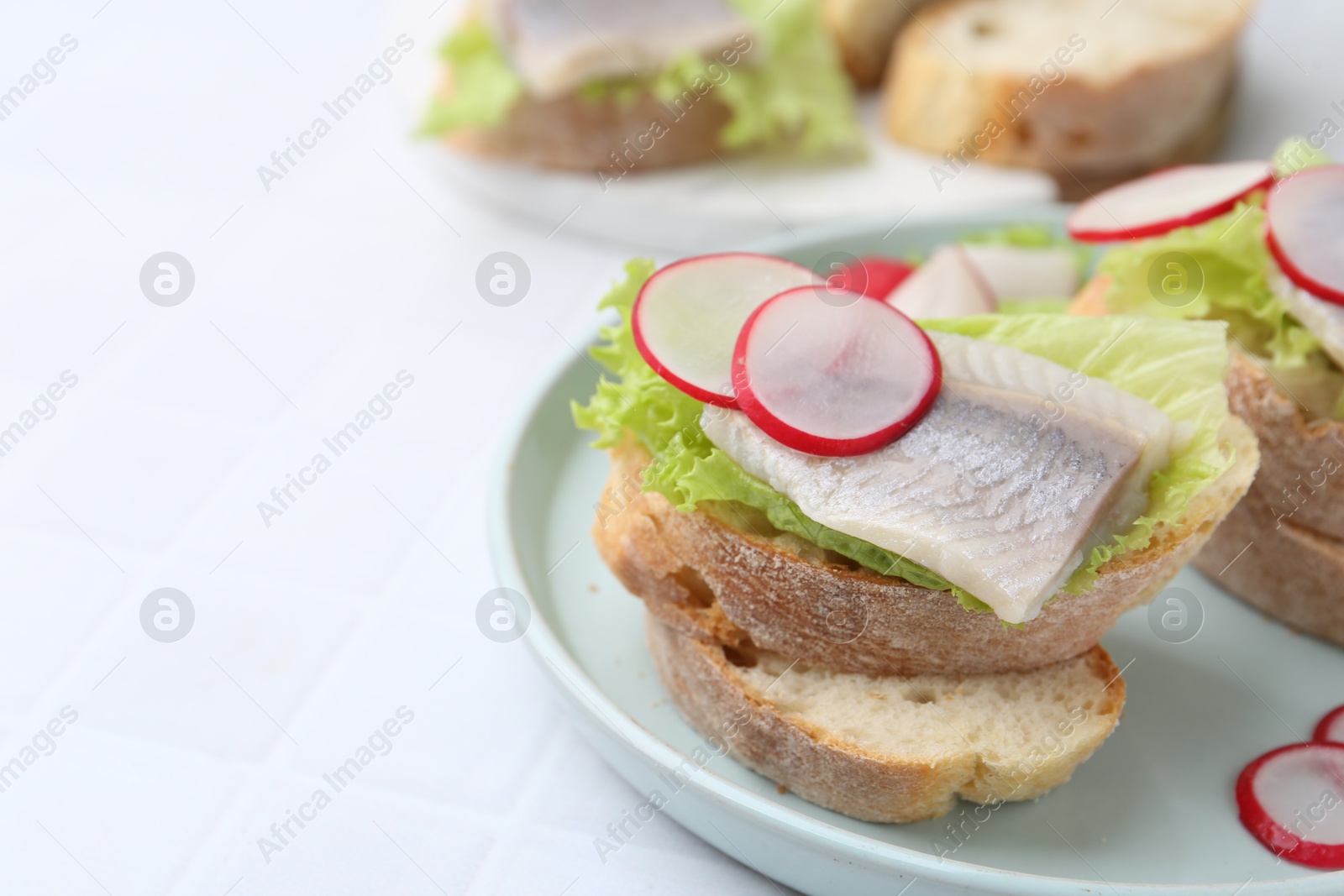 Photo of Tasty sandwiches with herring, radish and lettuce on white tiled table, closeup. Space for text