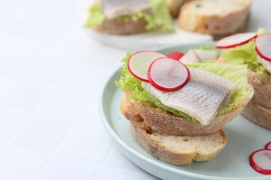 Photo of Tasty sandwiches with herring, radish and lettuce on white tiled table, closeup. Space for text