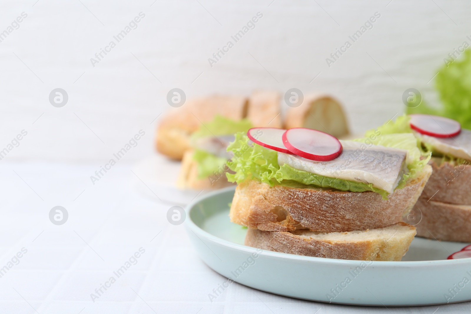 Photo of Tasty sandwiches with herring, radish and lettuce on white tiled table, closeup. Space for text