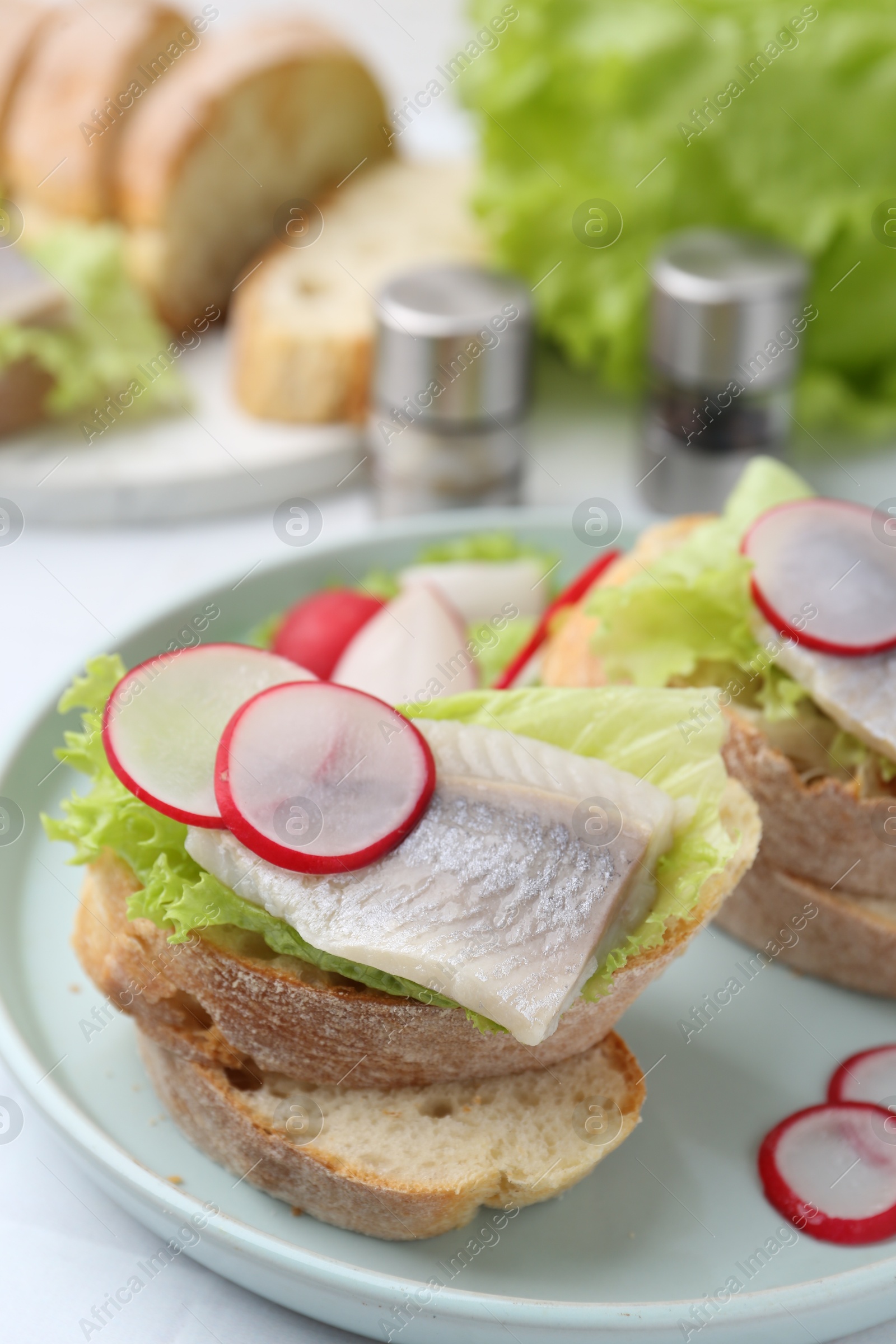 Photo of Tasty sandwiches with herring, radish and lettuce on table, closeup