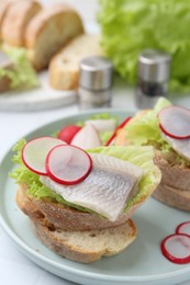 Photo of Tasty sandwiches with herring, radish and lettuce on table, closeup