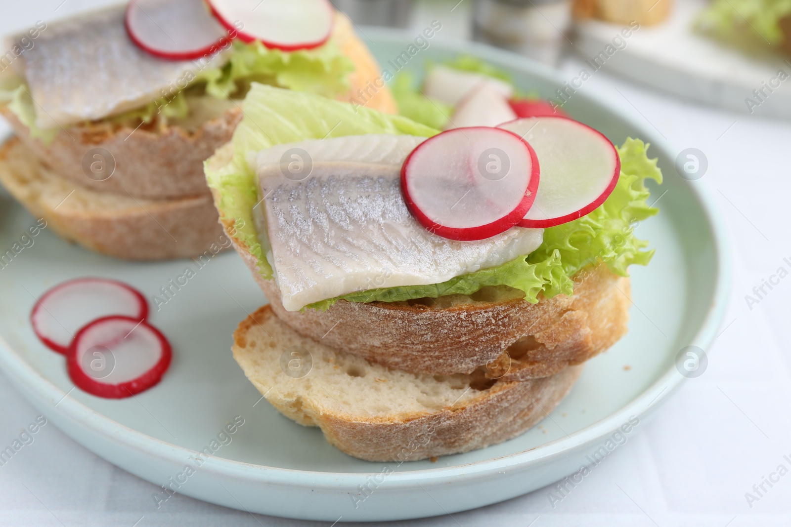 Photo of Tasty sandwiches with herring, radish and lettuce on white table, closeup