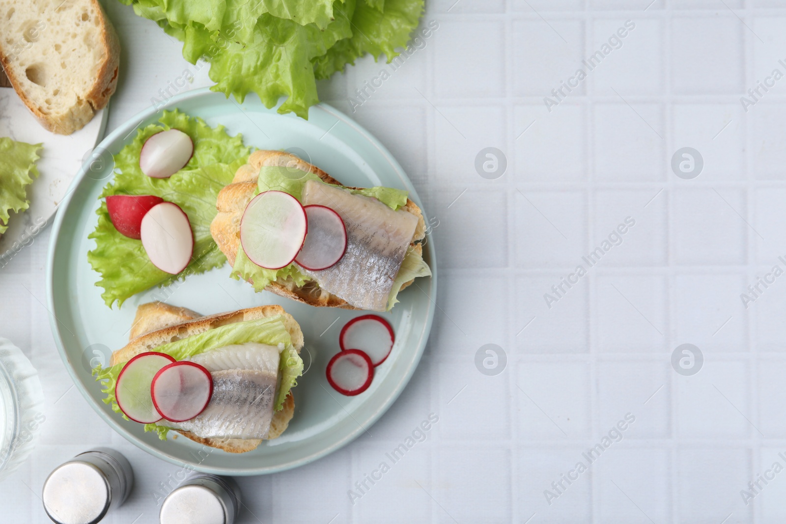 Photo of Tasty sandwiches with herring, radish and lettuce on white tiled table, flat lay. Space for text