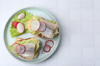 Photo of Tasty sandwiches with herring, radish and lettuce on white tiled table, top view. Space for text