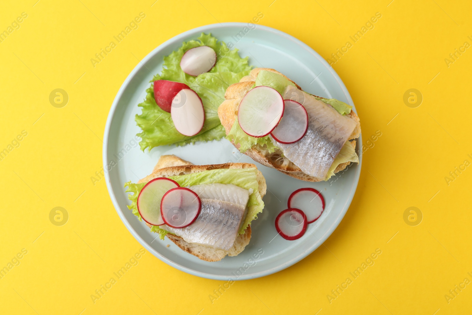 Photo of Tasty sandwiches with herring, radish and lettuce on yellow background, top view