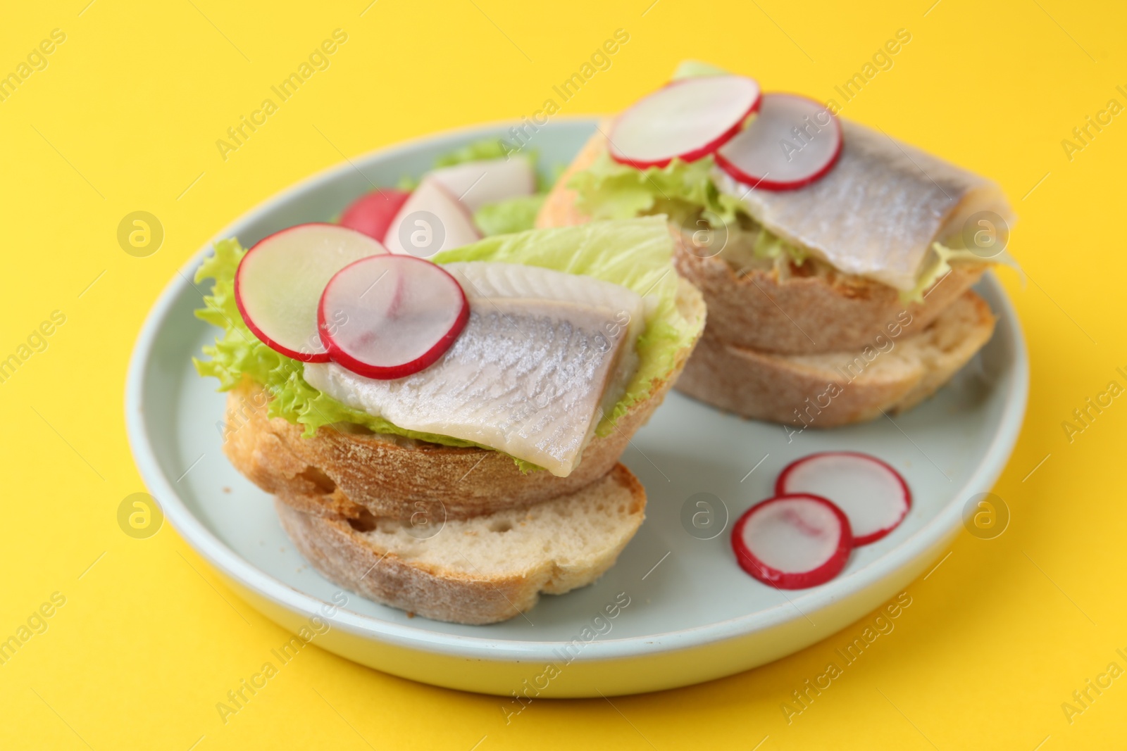 Photo of Tasty sandwiches with herring, radish and lettuce on yellow background, closeup