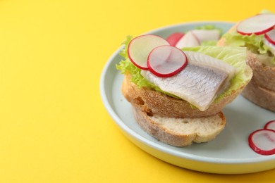 Photo of Tasty sandwiches with herring, radish and lettuce on yellow background, closeup. Space for text