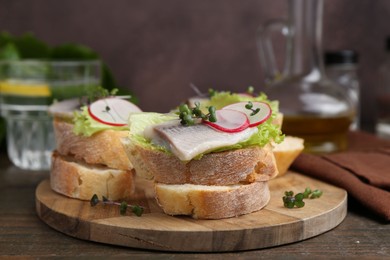 Photo of Tasty sandwiches with herring, radish and lettuce on wooden table, closeup