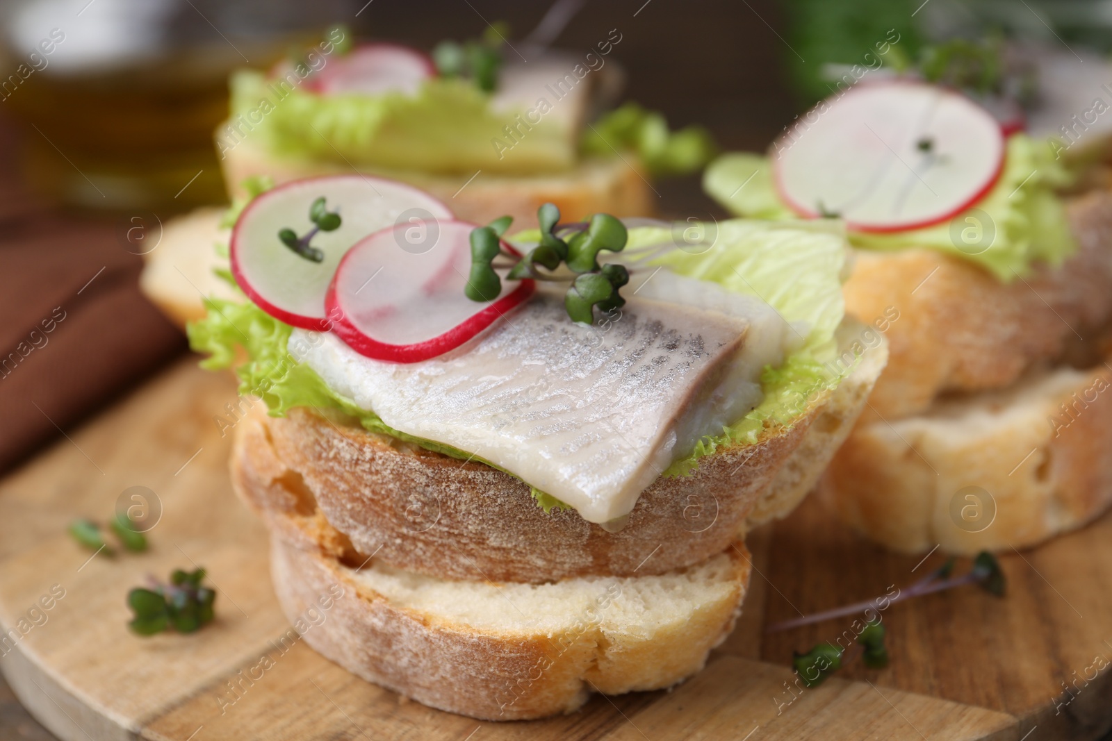 Photo of Tasty sandwiches with herring, radish and lettuce on table, closeup