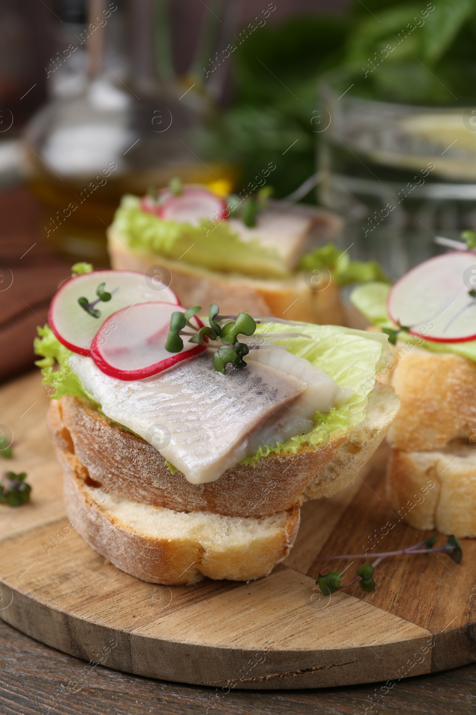 Photo of Tasty sandwiches with herring, radish and lettuce on wooden table, closeup