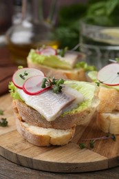 Tasty sandwiches with herring, radish and lettuce on wooden table, closeup