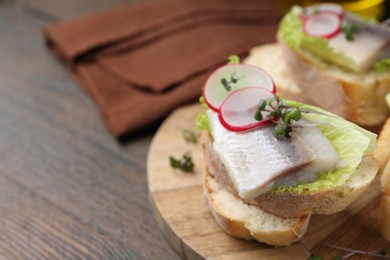 Photo of Tasty sandwiches with herring, radish and lettuce on wooden table, closeup. Space for text