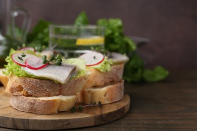 Photo of Tasty sandwiches with herring, radish and lettuce on wooden table, closeup. Space for text