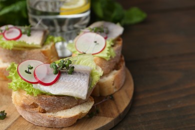 Photo of Tasty sandwiches with herring, radish and lettuce on wooden table, closeup. Space for text