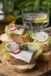 Photo of Tasty sandwiches with herring, radish and lettuce on table, closeup