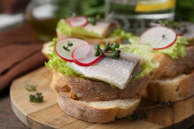 Photo of Tasty sandwiches with herring, radish and lettuce on table, closeup