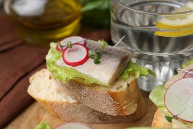 Photo of Tasty sandwiches with herring, radish and lettuce on table, closeup