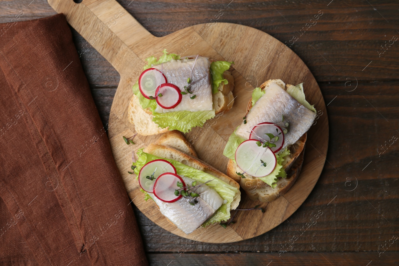 Photo of Tasty sandwiches with herring, radish and lettuce on wooden table, top view