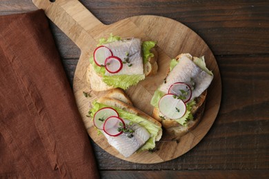 Photo of Tasty sandwiches with herring, radish and lettuce on wooden table, top view